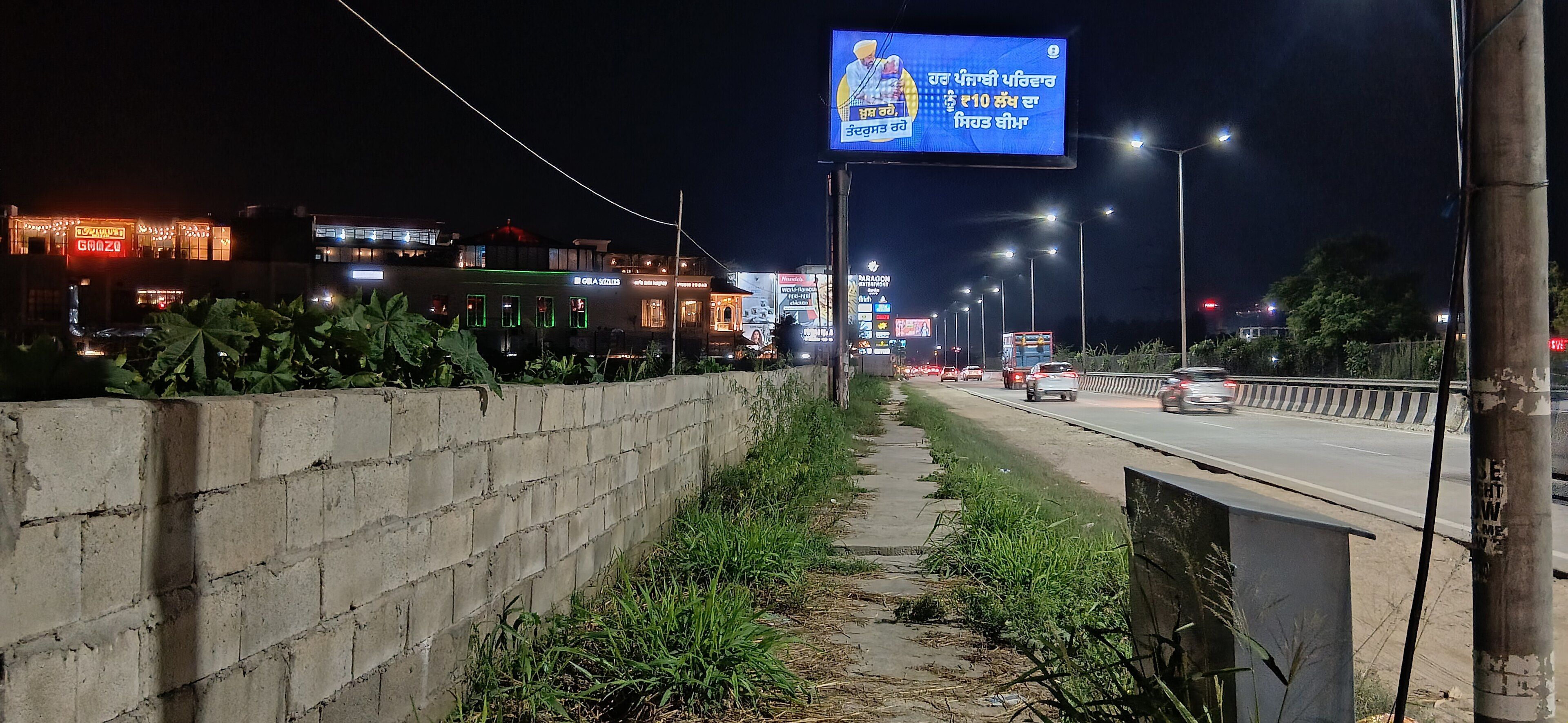 A lit hoarding beside Canal Road, Ludhiana, at night